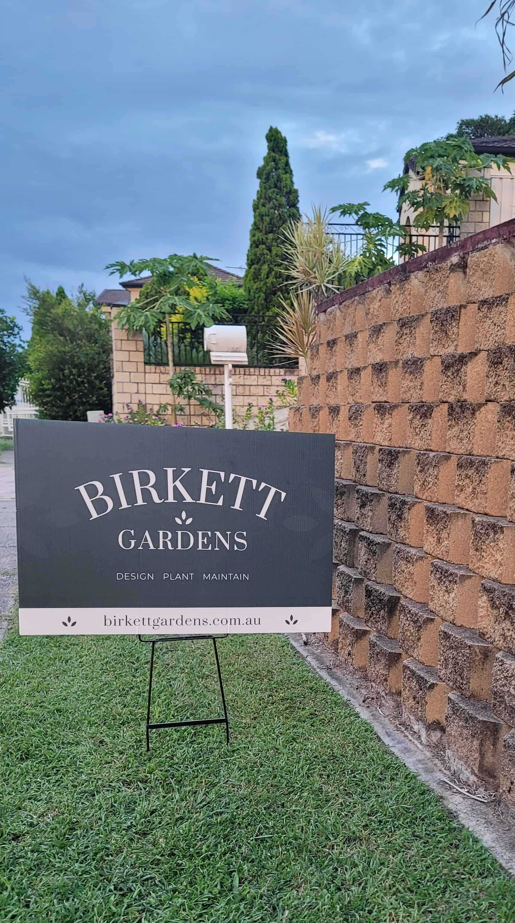 Birkett Gardens lawn sign sticking out of the lawn next to a garden retaining wall.