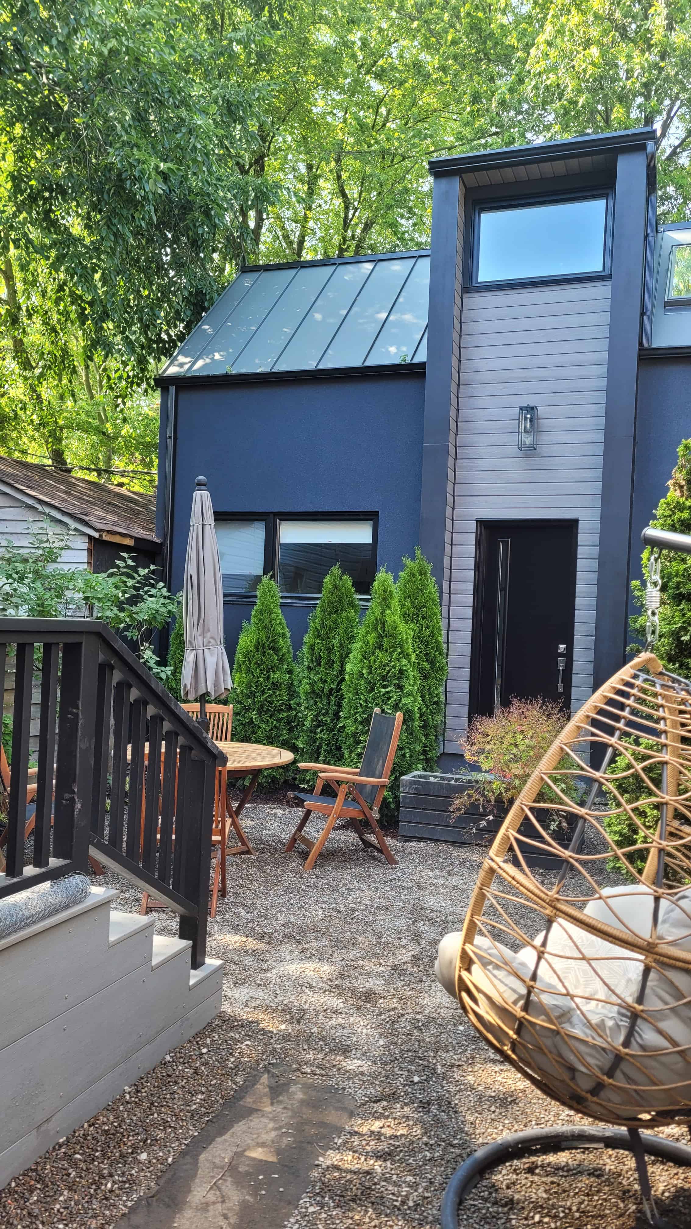 Relaxing outdoor space with swing chair, table, cedar hedge and gravel patio.