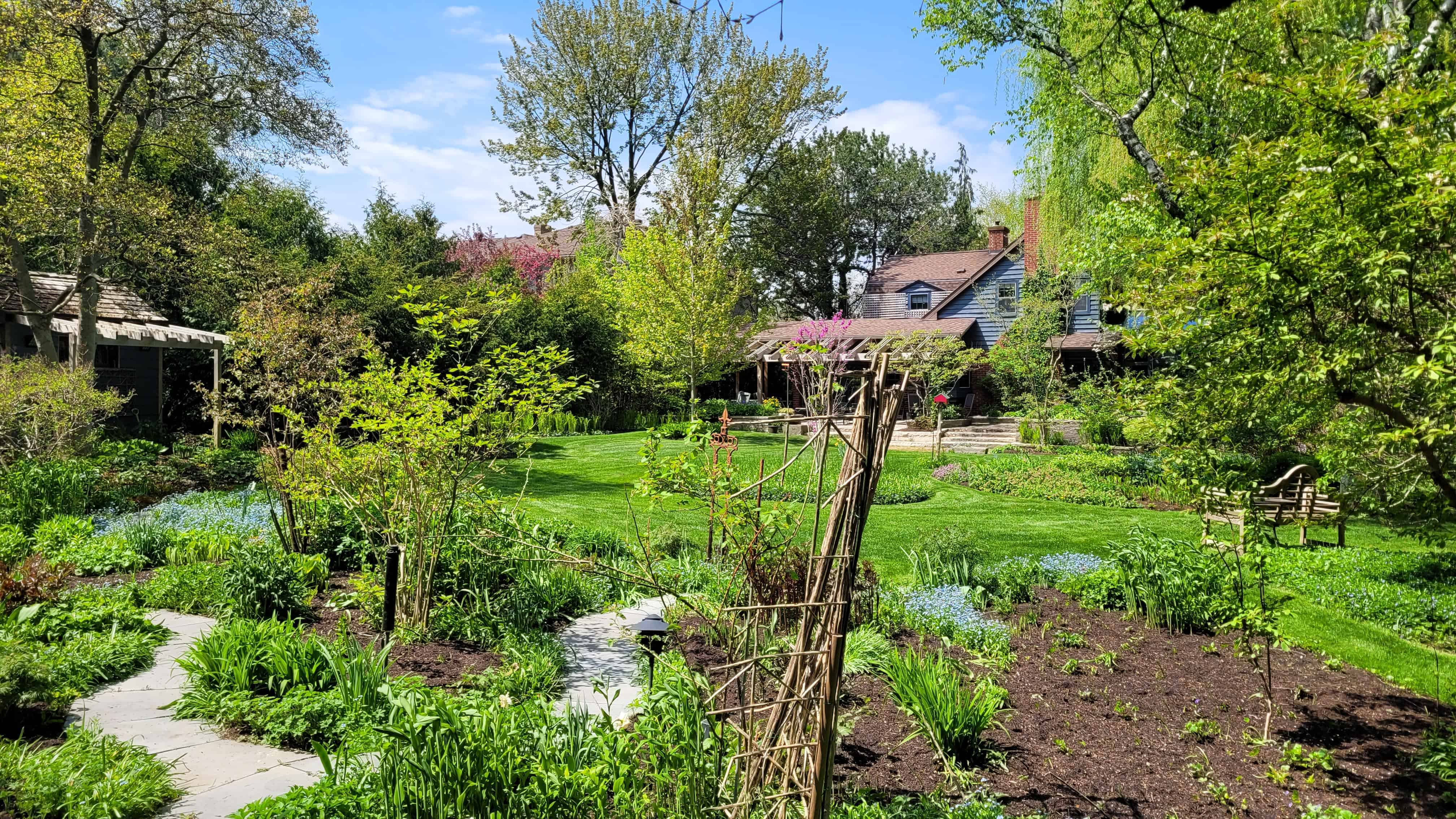 Tranquil perenial garden with walkway and distant house.