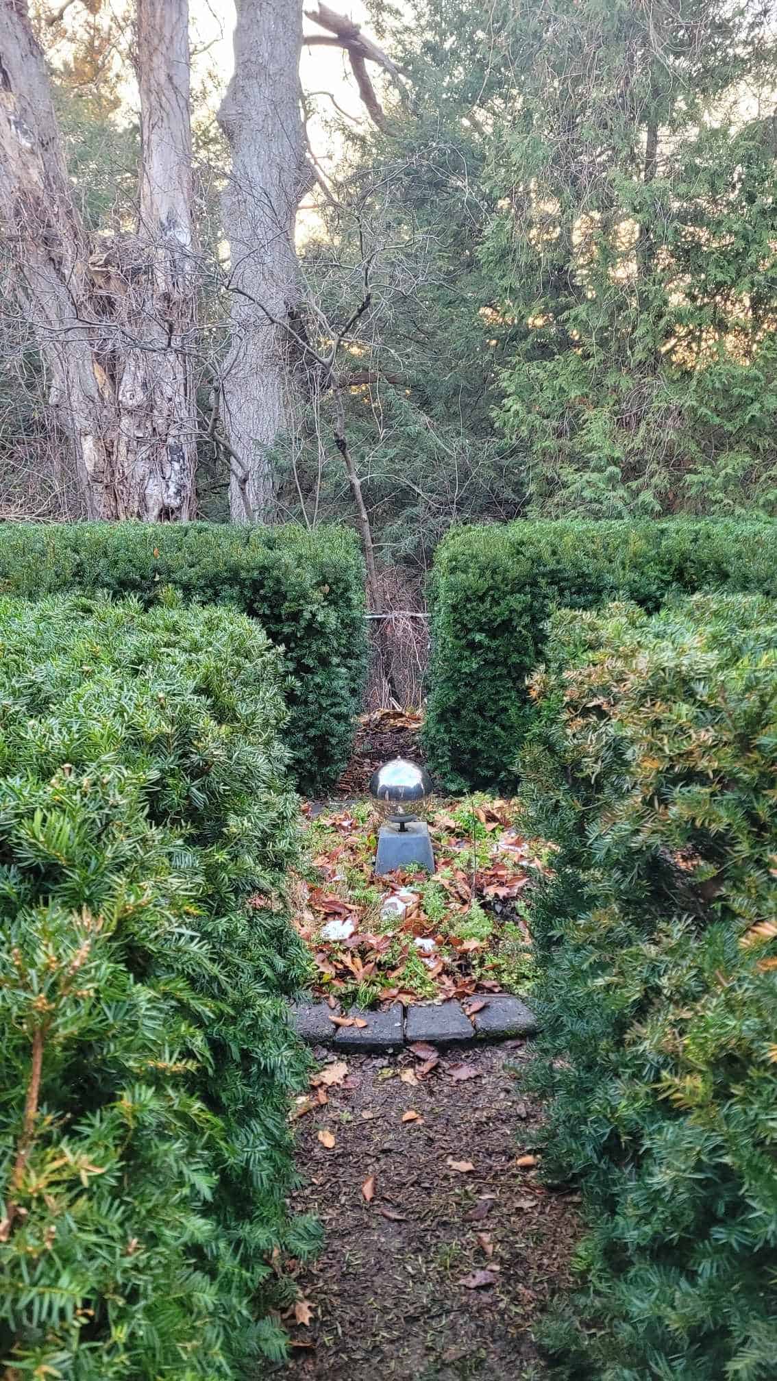 Neatly clipped yew hedges forming a border of boxes with an reflective art piece in the center.