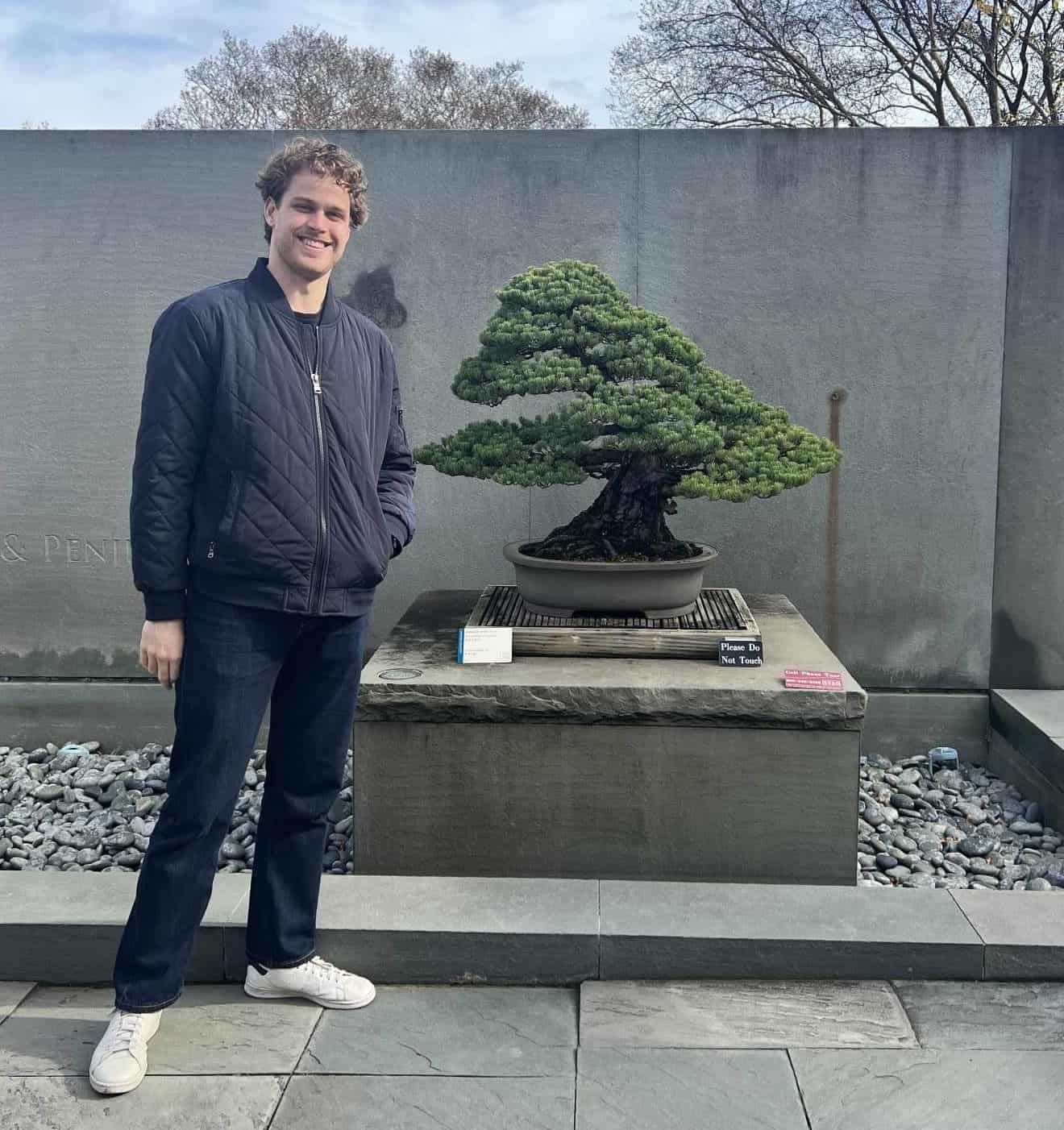 A man standing next to a bonsai tree, showcasing the harmony between nature and humans.